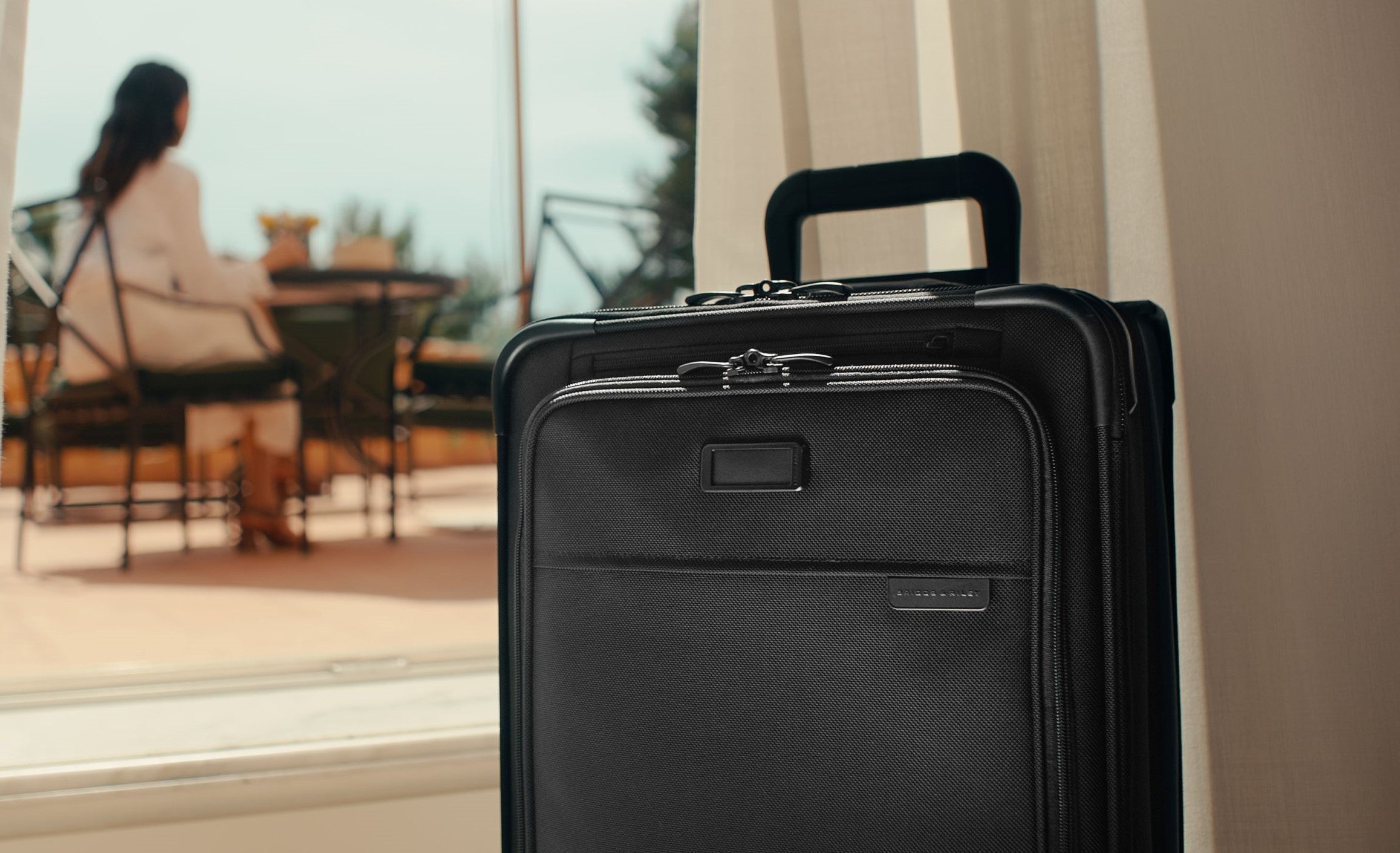 Essential carry-on spinner suitcase with woman in background 
