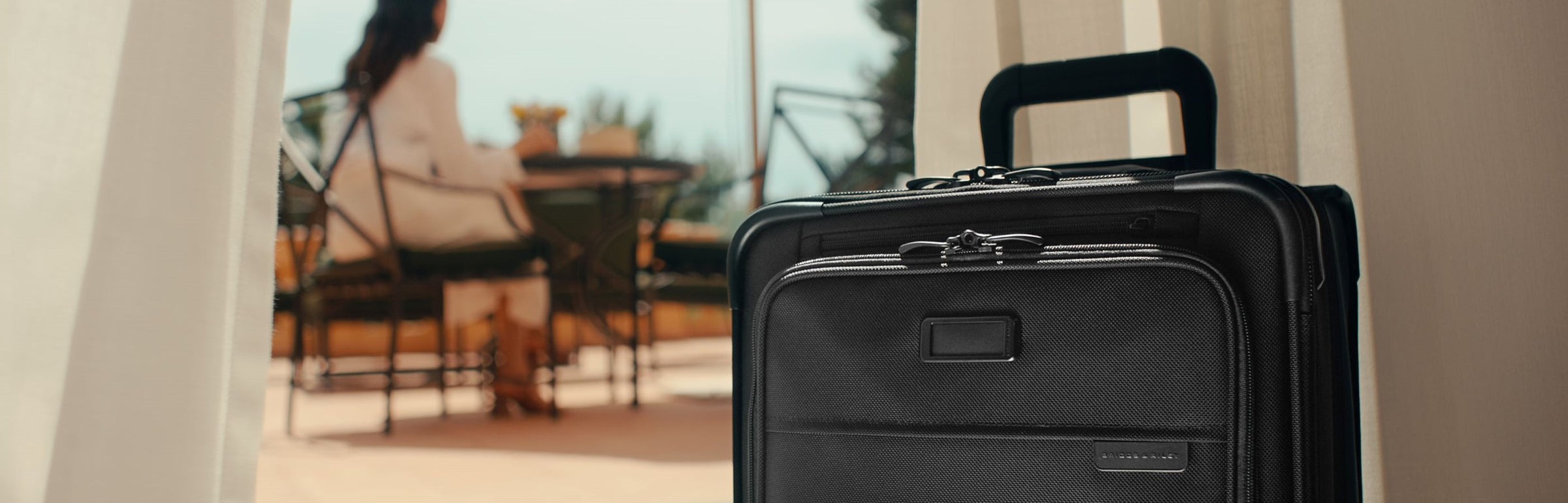 Essential carry-on spinner suitcase with woman in background 