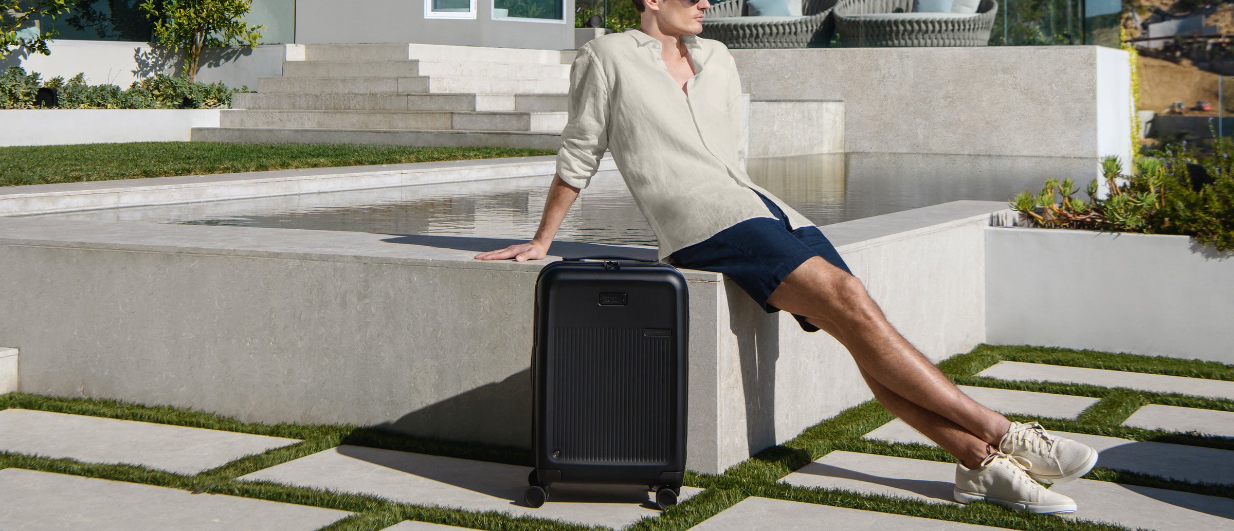Woman sitting on a stone ledge with a black suitcase in an outdoor setting