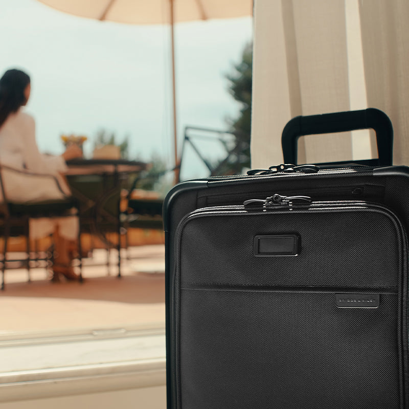Essential carry-on spinner suitcase with woman in background 