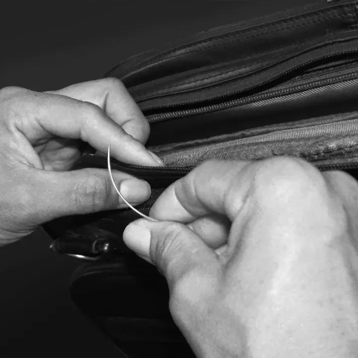 Hands repairing heavy-duty zipper seam on large suitcase